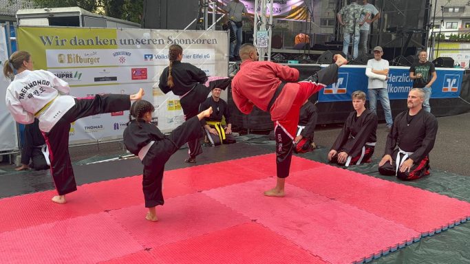 Kampfsport-Demonstration mit mehreren Teilnehmern auf einer roten Matte.