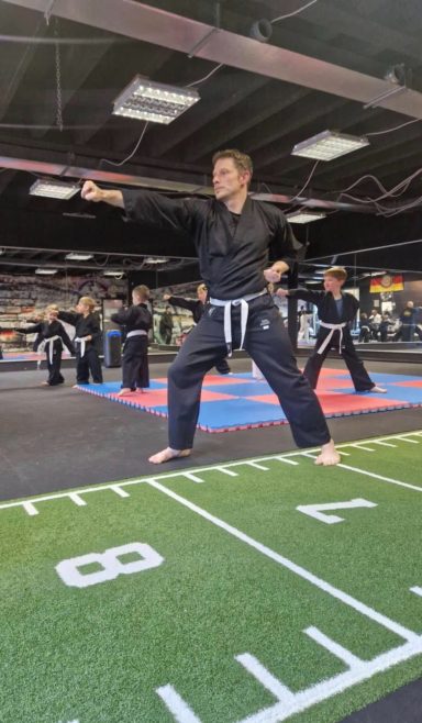 Ein Kämpfer in Schwarz mit Gürtel führt eine Technik im Trainingsraum aus.