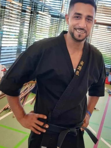 Mann in schwarzem Karateanzug lächelt mit den Händen in den Hüften.