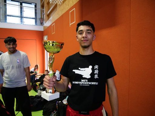 Mann in schwarzem T-Shirt hält einen Pokal in einer Sportumgebung.