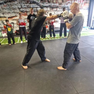 Ein Trainer zeigt einer Gruppe von Schülern einen Boxschlag im Trainingsraum.