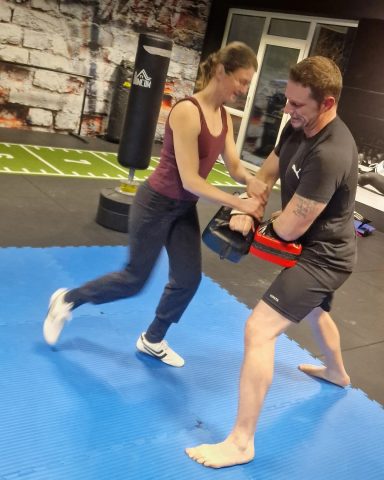 Zwei Personen trainieren zusammen in einem Fitnessstudio auf einer blauen Matte.