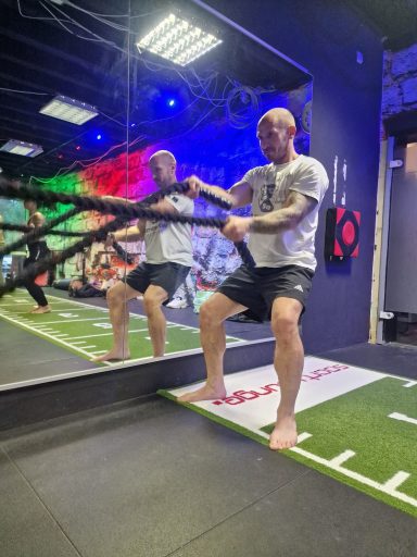 Person trainiert mit einem Seil in einem modernen Fitnessstudio, barfuß und vor einem Spiegel.