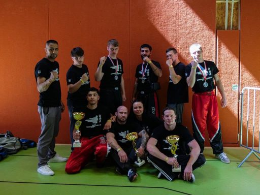 Gruppe von Sportlern in schwarzen T-Shirts, posierend mit Pokalen in einer Sporthalle.