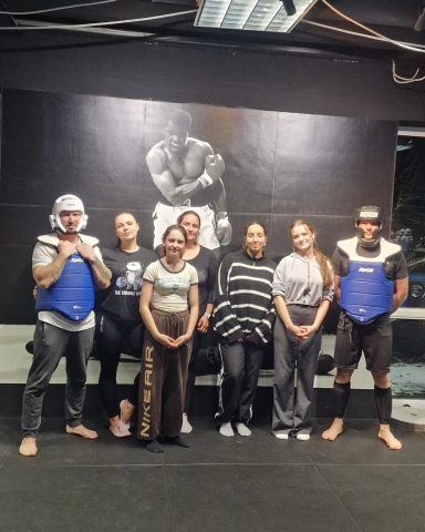 Gruppe von Kämpfern in Sportbekleidung stehen in einem Fitnessstudio vor einer Wandkunst.